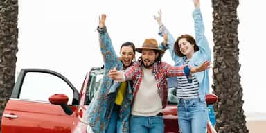 Young adults cheering with their rented vehicle, symbolizing the excitement of starting a new journey.