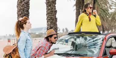 Three friends planning a road trip, looking at a map on the hood of a red convertible car.
