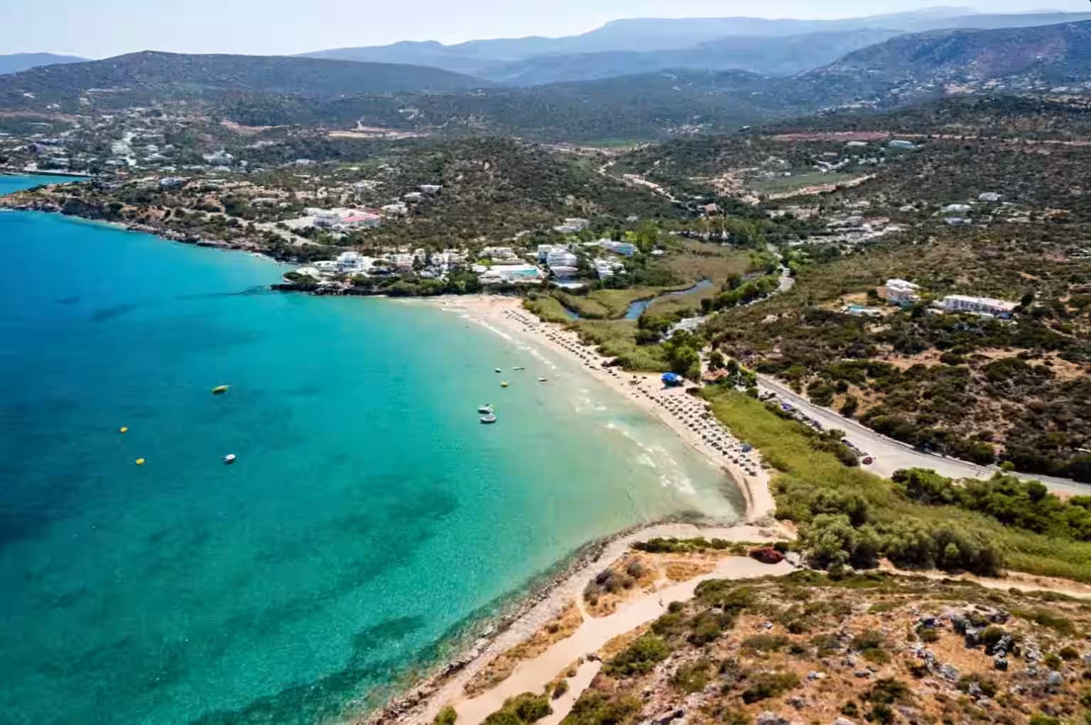 Aerial view of Almyros Beach and resort area, Heraklion, Crete, with clear turquoise water and a small river flowing into the sea