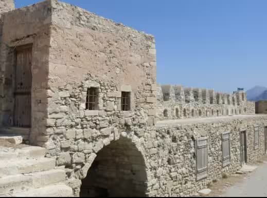 Historic Venetian Kales Fortress in Ierapetra, Crete, showing rough stone walls, arched passageway, small windows, and crenellated ramparts under a clear blue sky.