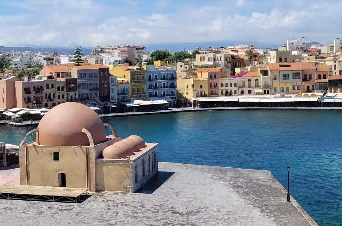 The Giali Tzamisi Mosque (Küçük Hasan Pasha Mosque) on the quay of the Venetian Old Harbor of Chania, Crete, with colorful waterfront buildings in the background