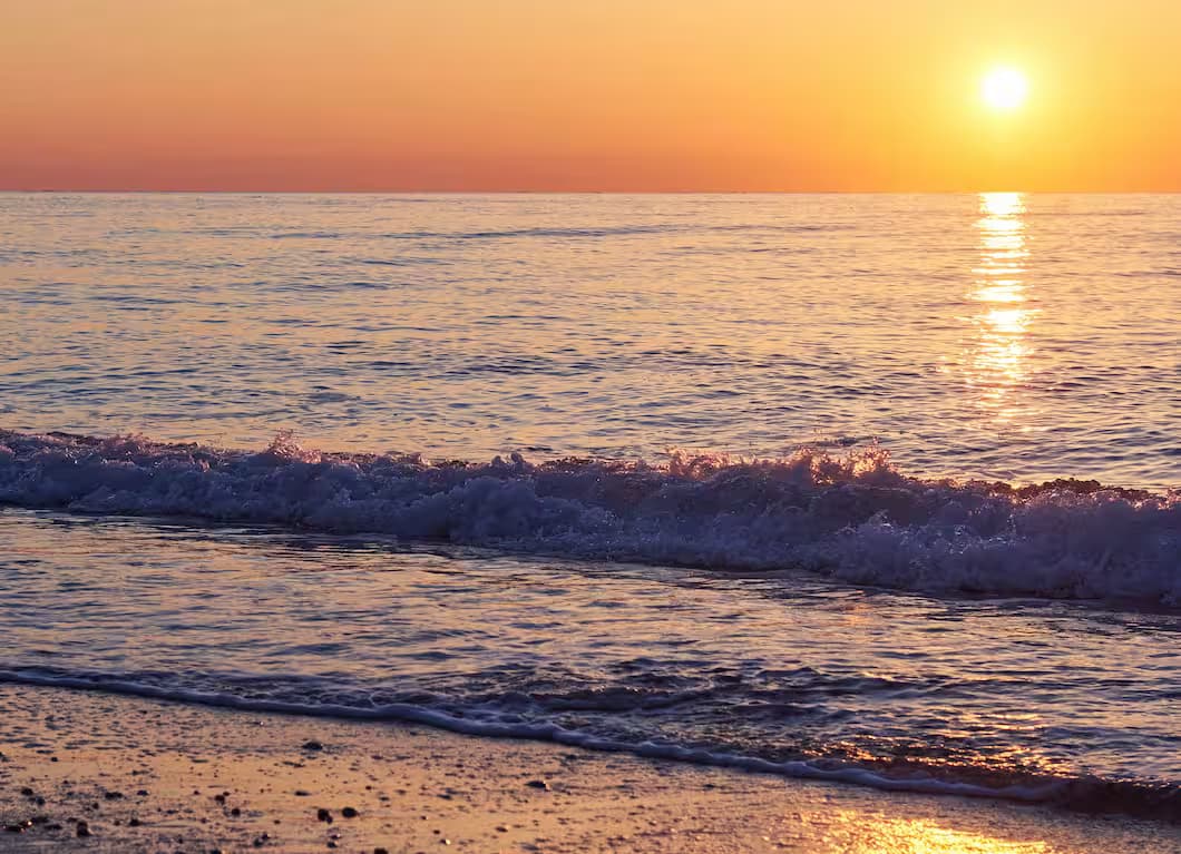 Golden sunset colors reflecting on the Mediterranean sea surface as a wave rolls onto a sandy beach in Crete, Greece