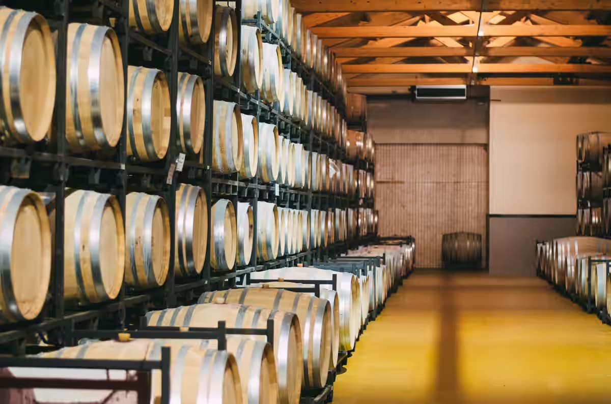 Rows of aging wooden oak barrels stacked in a modern wine cellar or Cretan distillery, representing local wine and Raki production in Crete, Greece