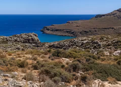 Dramatic arid landscape and high cliffs overlooking a remote, clear blue cove near Zakros, East Crete, Greece